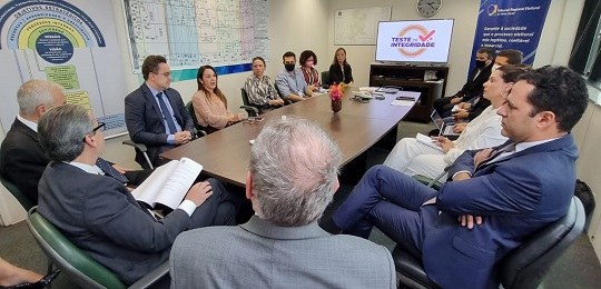 Várias mulheres e homens sentados ao redor de uma mesa de reunião.