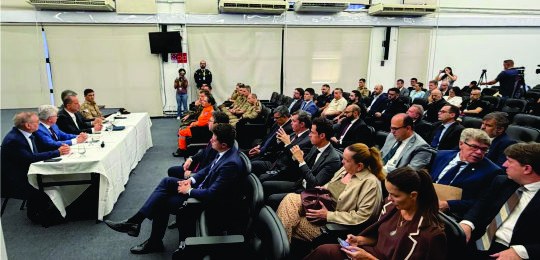 instalação GIS Eleições 2026 No canto esquerdo, cinco homens sentados junto a uma mesa. À frente deles, várias pessoas na pla...