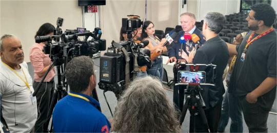 instalação GIS Eleições 2026 Desembargador Paulo Tamburini cercado por jornalistas. Alguns seguram microfones junto ao desemb...