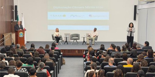 Foto do juiz Auro Aparecido Maia de Andrade durante discurso, em um auditório com plateia lotada.