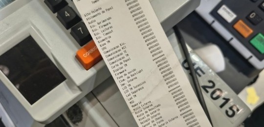 Foto tirada do alto mostra três mulheres junto a bancadas com dezenas de urnas eletrônicas