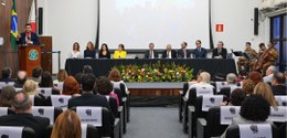 Auditório lotado. Ao fundo, autoridades sentadas atrás de uma mesa e juiz Matheus Miranda de pé ...