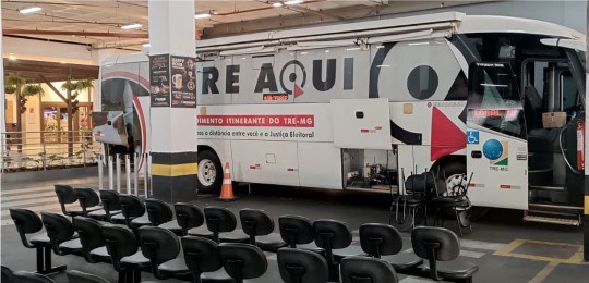 ônibus TRE Aqui Minas Shopping Foto mostra um ônibus com plotagem TRE Aqui, em um estacionamento coberto.
