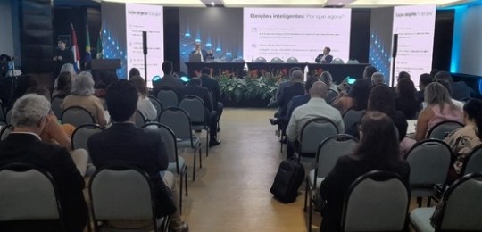 Fota mostra homens e mulheres sentados ao redor de uma grande mesa em formato de U.