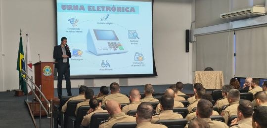 Wellerson Amarante, secretário de TI do TRE-MG, durante palestra. Junto dele há um telão com inf...