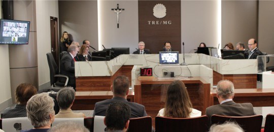 Em primeiro plano, parte de uma plateia, com pessoas de costas para a câmera. Ao fundo, juízes e...