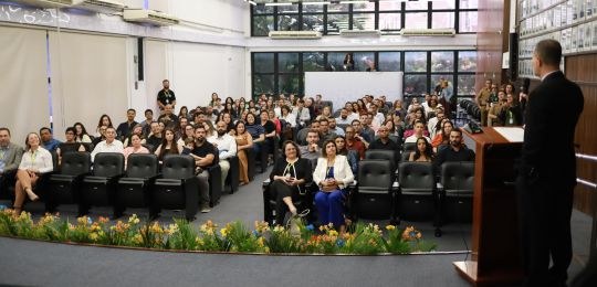 Foto mostra a plateia de um auditório. As pessoas olham para o desembargador Júlio César Lorens,...