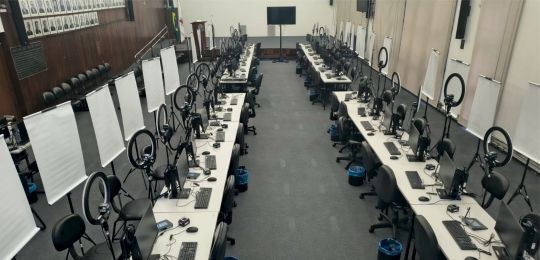 Foto mostra diversos guichês de atendimento ao eleitor montados dentro de um auditório. O espaço...