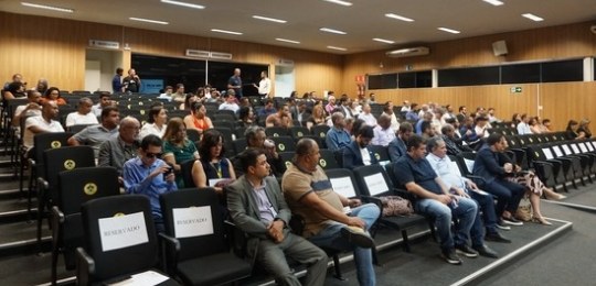 Foto da plateia de um auditório, com várias pessoas sentadas.