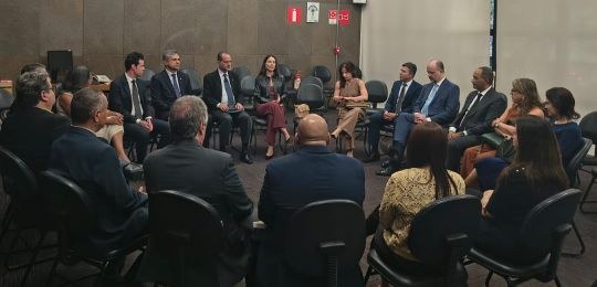 Foto mostra homens e mulheres sentados em cadeiras formando um círculo. Todos vestem roupas formais