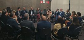 Foto mostra homens e mulheres sentados em cadeiras formando um círculo. Todos vestem roupas formais