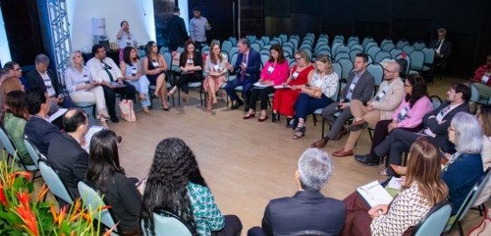 Fota mostra homens e mulheres sentados ao redor de uma grande mesa em formato de U.