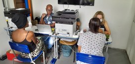 Rua de Direitos CIAM Duas mulheres, de costas para a câmera, são atendidas por servidores do TRE.