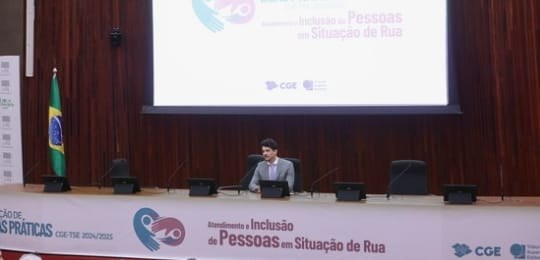 Servidor Emerson Matos, do TRE-MG, durante apresentação. Ele veste terno cinza claro e está sent...