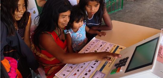 Diversos indígenas observam cartazes colados na parede de uma escola.