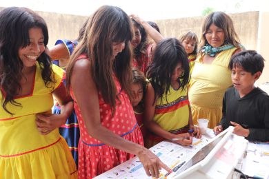 Diversos indígenas observam cartazes colados na parede de uma escola.