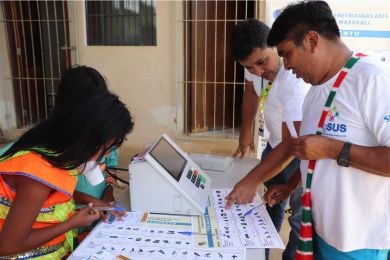 Diversos indígenas observam cartazes colados na parede de uma escola.