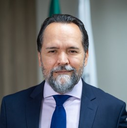 Foto do Desembargador Ramom Tácio. Homem branco de terno azul marinho, camisa branca, gravata az...