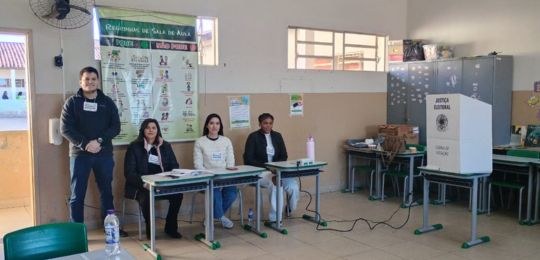 Fotos de pessoas quatro pessoas em uma seção eleitoral, sendo uma em pé e três sentadas, prepara...