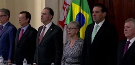 Foto de autoridades de pé à frente de duas bandeiras