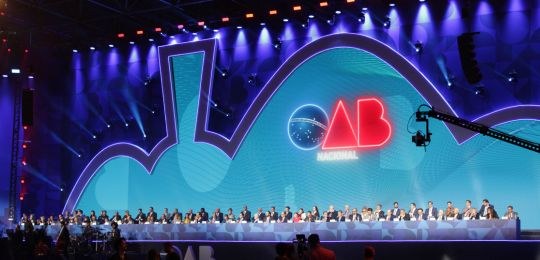 Foto de evento da OAB com mesa de honra composta  e fundo azul