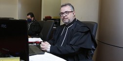 Foto do juiz Luiz Carlos Rezende e Santos sentado na mesa da Sala de Sessões do TRE-MG. Ele está...