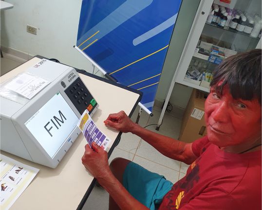 A imagem mostra um indígena maxakali votando em uma urna eletrônica.