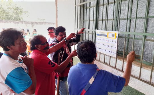 A imagem mostra indígenas maxakali consultando os candidatos da eleição parametrizada em um cartaz.