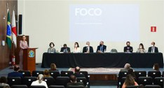 Foto de mesa de autoridades no auditório do TRE. A ministra Maria Claudia Bucchianeri está de pé...