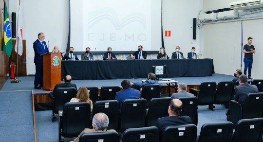 Desembargador Marcos Lincoln dos Santos de pé, à esquerda. Ao fundo, autoridades sentadas atrás ...