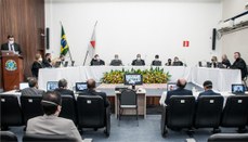 Foto que mostra a mesa de honra de uma solenidade, com diversas autoridades sentadas ao redor de...