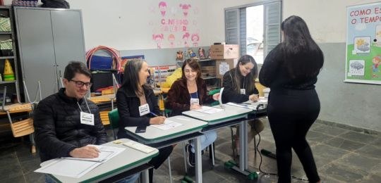 Fotos de quatro pessoas sentadas,  em uma seção eleitoral, e uma eleitora em pé sendo atendida.
