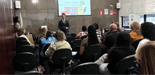 Foto mostra o juiz Ronaldo Borges, de pé, ao fundo. Em primeiro plano, pessoas sentadas na plate...