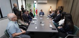 Sala com onze pessoas sentadas à mesa e três pessoas de pé
