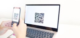 Imagem de um celular escaneando um QR code na tela de um computador.